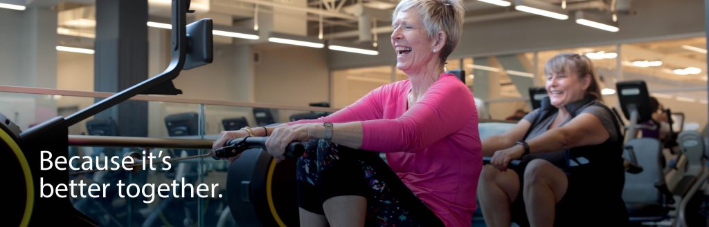 Because it's better together. Two older woman using rowing machines.