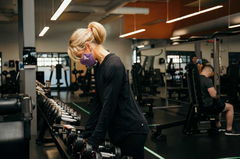 Woman with mask on using weights at the gym