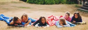 Young girls laying in grass in sleeping bags smiling
