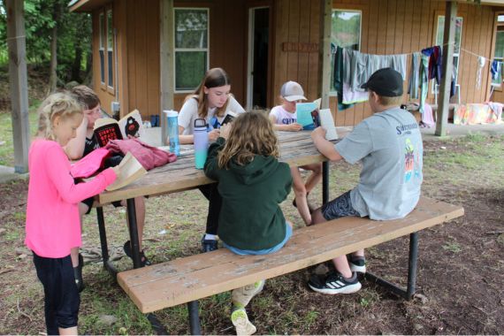 Group of boys and girls reading while sitting at picnic table