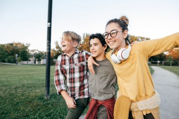 three children with arms around each other walking through park